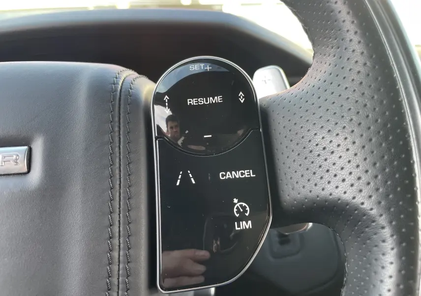 Gros plan sur les commandes du régulateur de vitesse au volant en cuir noir perforé du Range Rover Velar 2019.