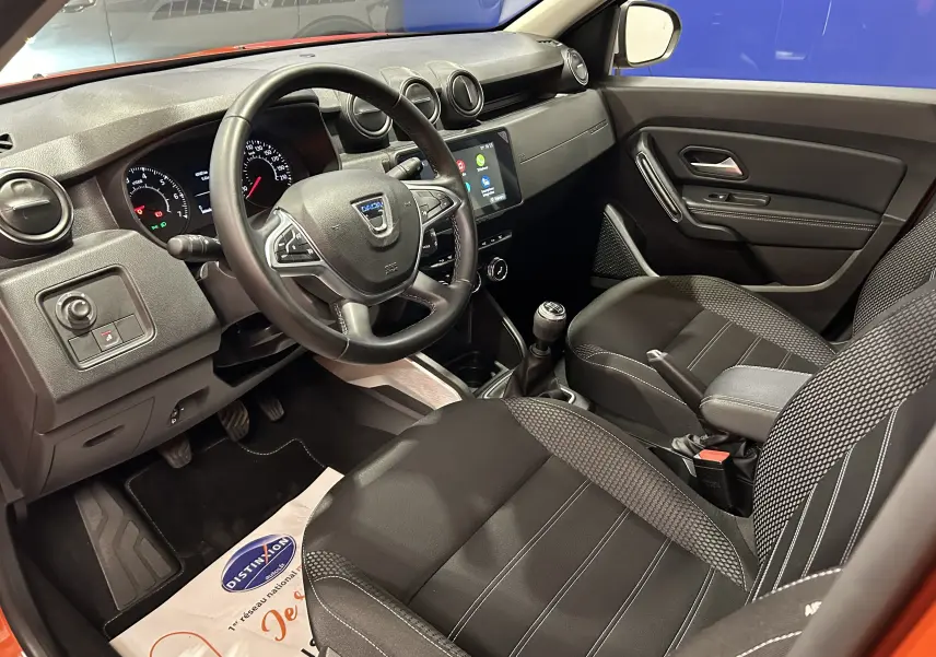 Intérieur du Dacia Duster 2022 orange Arizona, vue côté conducteur montrant le tableau de bord et les sièges en tissu noir.