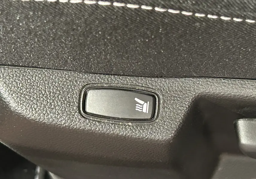 Bouton de siège chauffant en gros plan sur la garniture intérieure noire du Dacia Duster orange Arizona 2022.