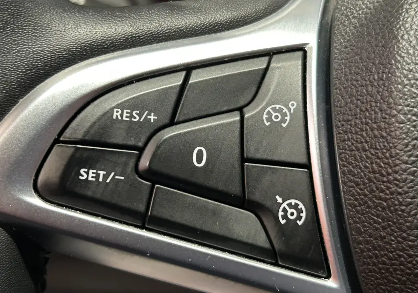 Gros plan sur les commandes de régulateur de vitesse du volant du Dacia Duster 2022, finition noire et argentée.