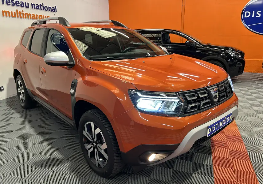 Dacia Duster orange Arizona en 3/4 avant droit avec phares allumés et jantes alliage distinctives.