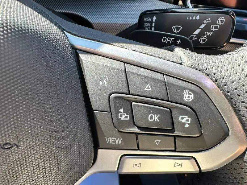 Gros plan sur les commandes du volant noir de la Volkswagen Golf 1.5 eTSI R-Line Edition 2025 avec boutons multifonctions et volant chauffant.