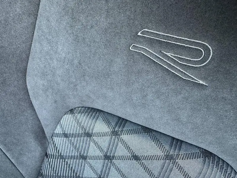 Gros plan sur la sellerie intérieure de la Volkswagen Golf 1.5 eTSI R-Line 2025, avec logo "R" brodé et tissu à motif géométrique.