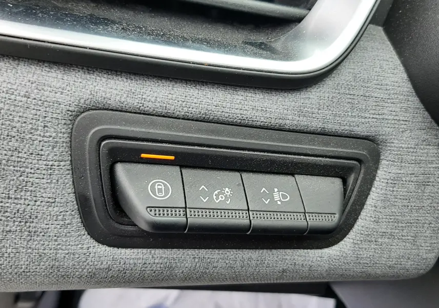 Gros plan sur les commandes de réglage des phares et du tableau de bord dans une Renault Clio V gris schiste, côté conducteur.