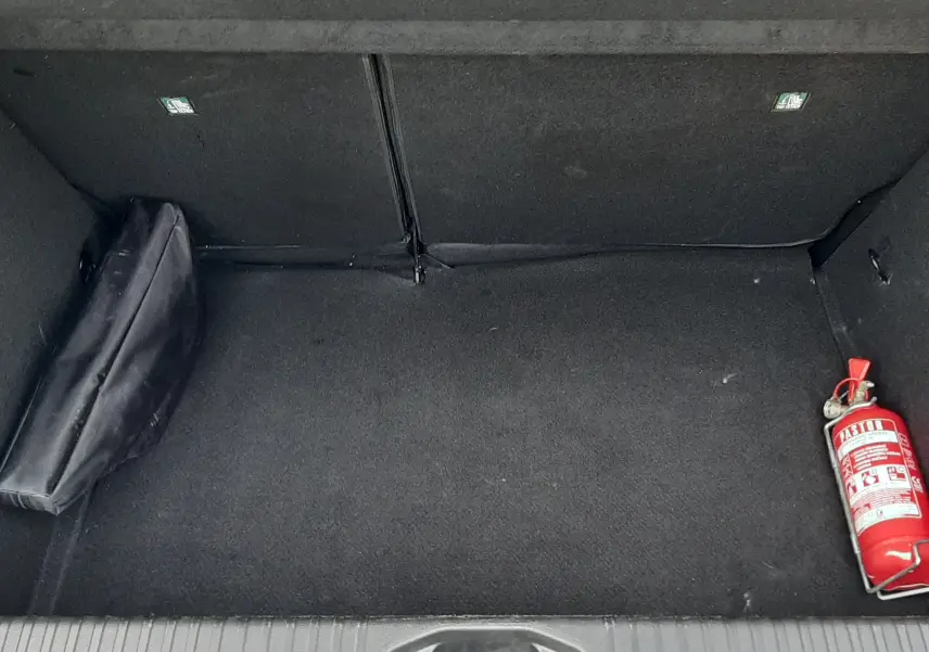 Coffre ouvert d'une Renault Clio V gris schiste, montrant un extincteur rouge et une trousse noire sur la moquette.