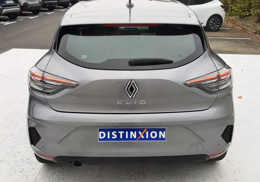 Vue arrière d'une Renault Clio V gris schiste avec feux LED et logo distinctif sur un parking extérieur.