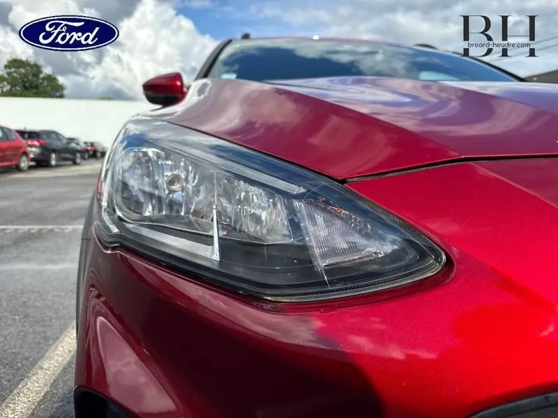 Gros plan sur le phare avant gauche d'une Ford Focus 1.0 EcoBoost rouge Premium Candy, avec reflet du ciel.