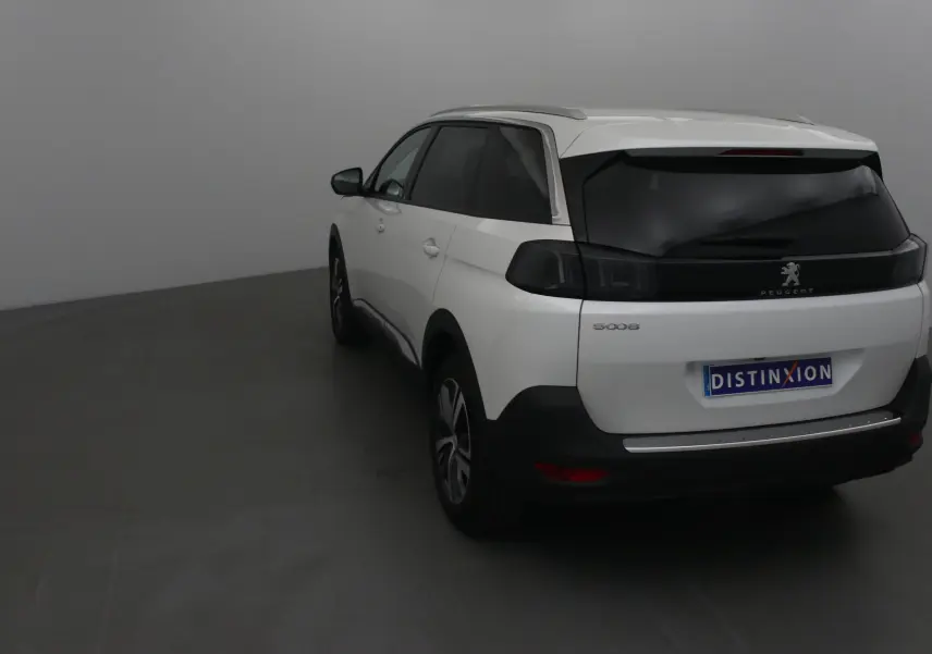 Vue 3/4 arrière gauche d'un Peugeot 5008 blanc nacré avec vitres teintées et feux arrière noirs dans un studio.