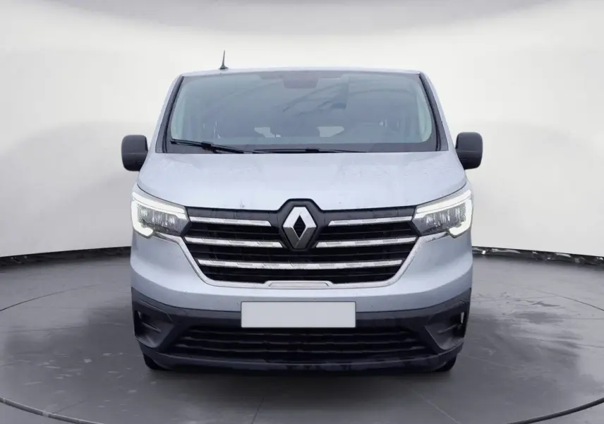 Vue frontale d'un Renault Trafic Combi gris clair métal 2023 avec calandre noire et phares allumés.