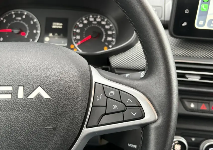 Gros plan sur le volant à droite avec commandes multifonctions du Dacia Jogger 2025, intérieur noir et tableau de bord visible.