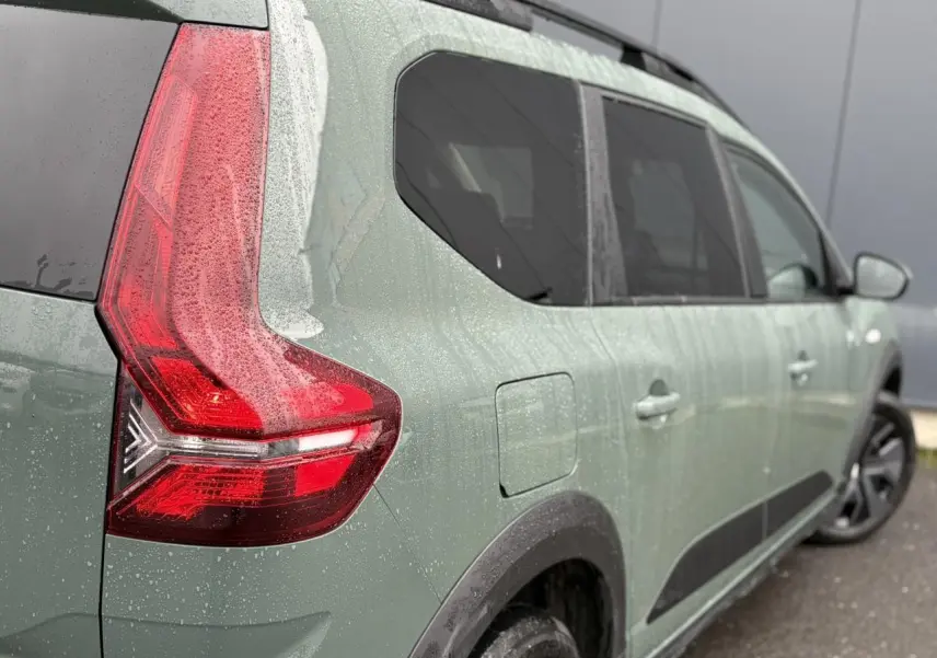 Vue 3/4 arrière droite du Dacia Jogger 2025 en kaki lichen avec feux arrière LED et barres de toit visibles.