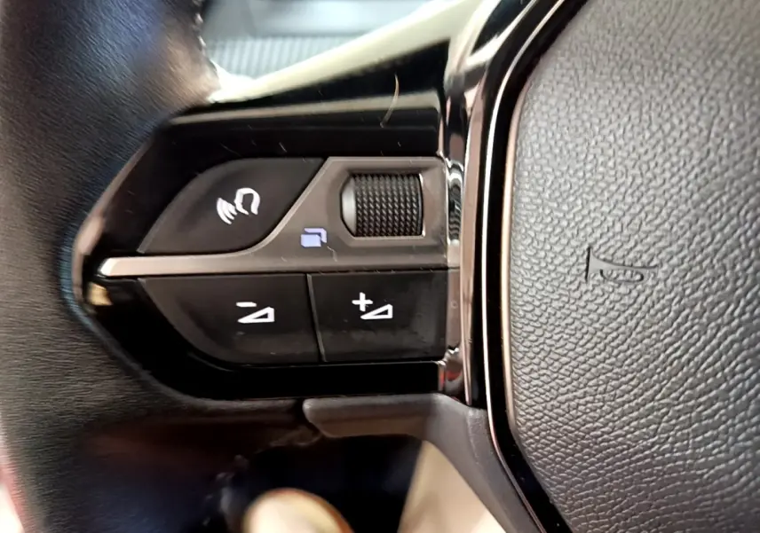 Gros plan sur les commandes vocales et volume au volant cuir noir de la Peugeot 208 électrique blanche.