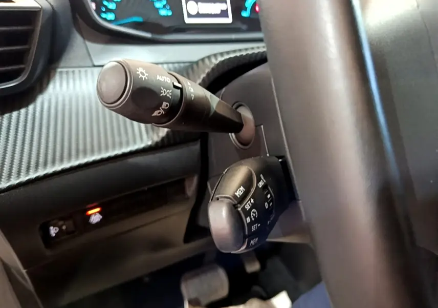 Gros plan sur la colonne de direction et commandes au volant d’une Peugeot 208 électrique blanche, version Active Business.