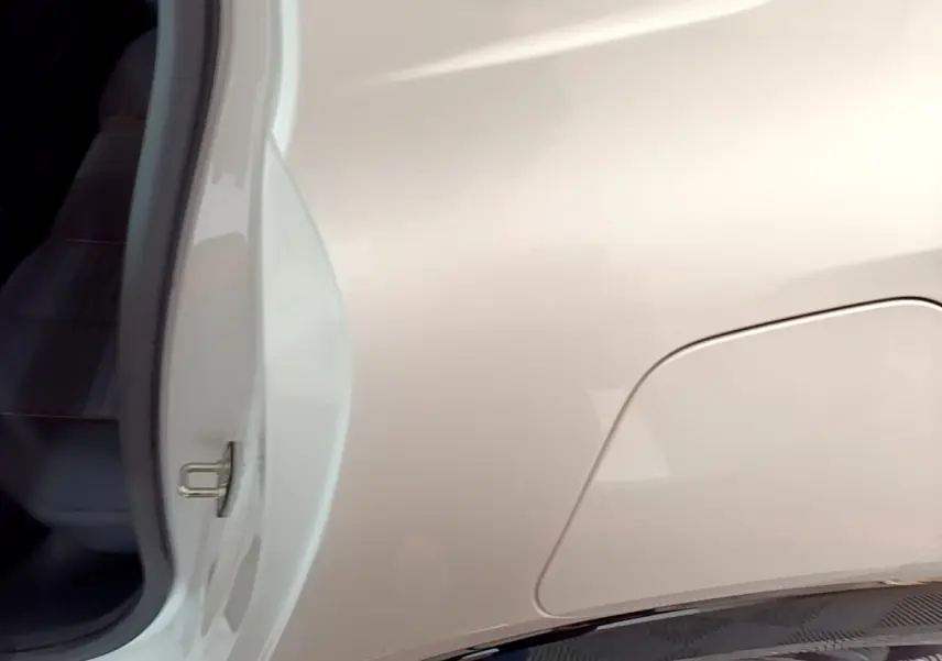 Vue rapprochée côté gauche arrière d’une Peugeot 208 électrique blanche, avec trappe de recharge visible.