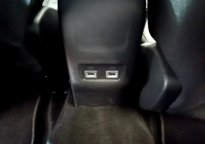 Vue rapprochée des ports USB arrière entre les sièges noirs d'une Peugeot 208 électrique blanche.