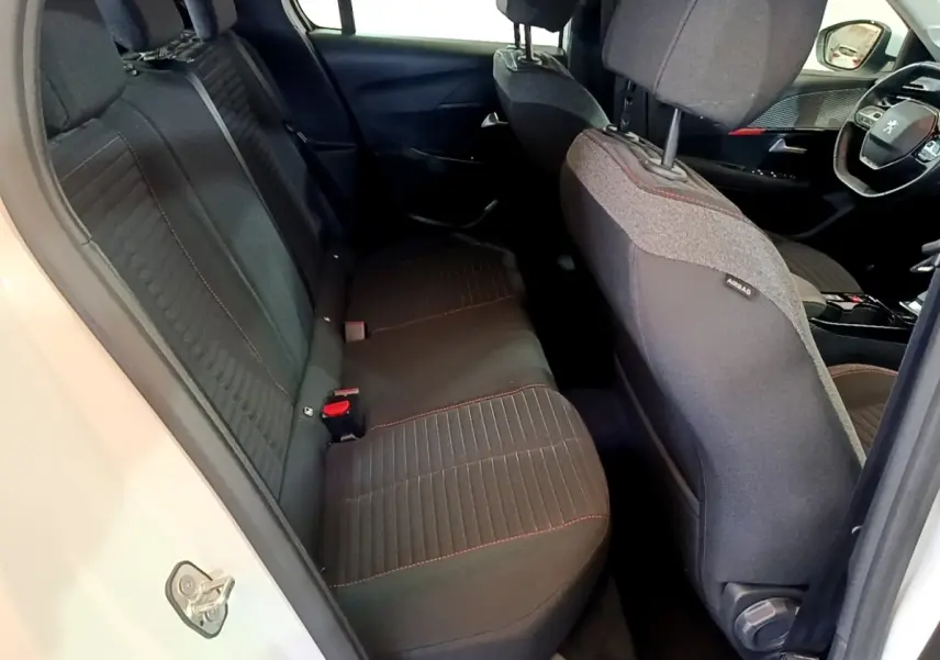 Vue intérieure côté arrière gauche du Peugeot 208 Electrique Active Business blanc, sièges tissu noir avec surpiqûres rouges.