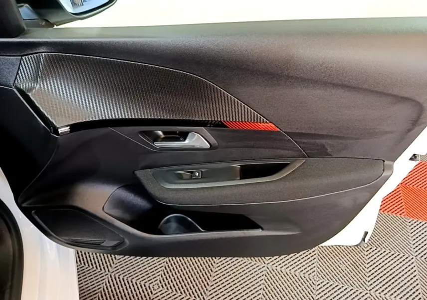 Vue intérieure côté gauche de la porte avant blanche du Peugeot 208 électrique avec insert carbone et détail rouge.