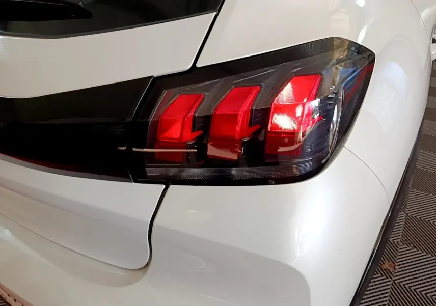 Gros plan sur le feu arrière droit rouge et noir d'une Peugeot 208 électrique blanche, version Active Business.
