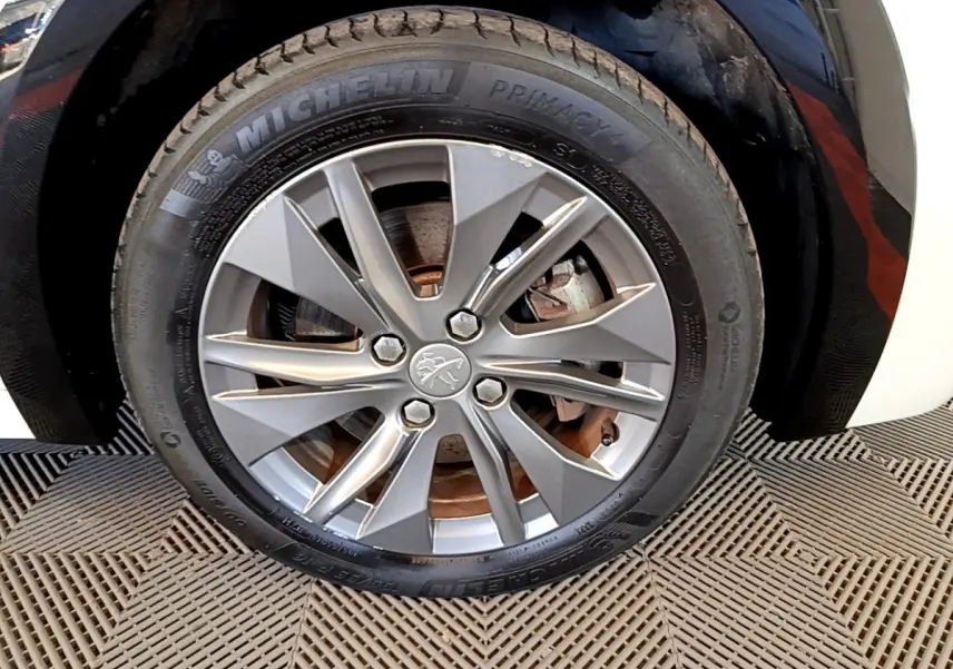 Gros plan sur la roue avant droite de la Peugeot 208 électrique blanche, jante alliage gris à 10 branches.