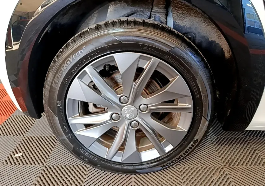 Gros plan sur la roue avant gauche de la Peugeot 208 électrique blanche, mettant en valeur la jante alu et le logo lion central.