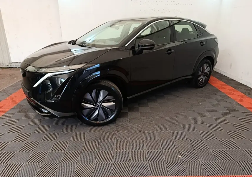 Nissan Ariya 63kWh noir en 3/4 avant droit, avec jantes modernes et lignes fluides dans un espace intérieur.