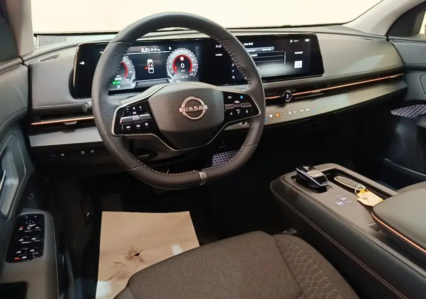 Vue intérieure avant du Nissan Ariya 63kWh noir, avec volant cuir multifonctions et grand écran tactile panoramique.