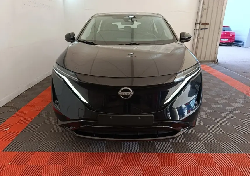 Vue de face d'une Nissan Ariya noire 2026 avec phares LED fins et calandre lisse dans un garage.