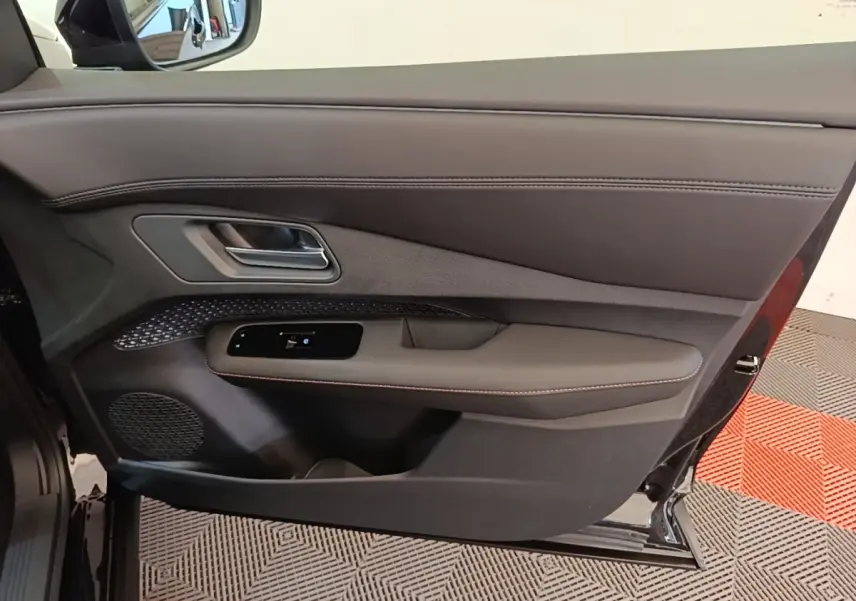 Vue intérieure côté gauche de la porte avant noire du Nissan Ariya 63kWh avec garniture cuir et commande vitres.
