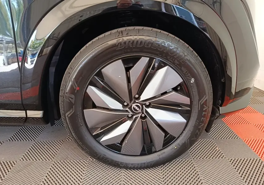 Gros plan sur la roue avant droite du Nissan Ariya noir, mettant en valeur la jante design bicolore et le pneu Bridgestone.
