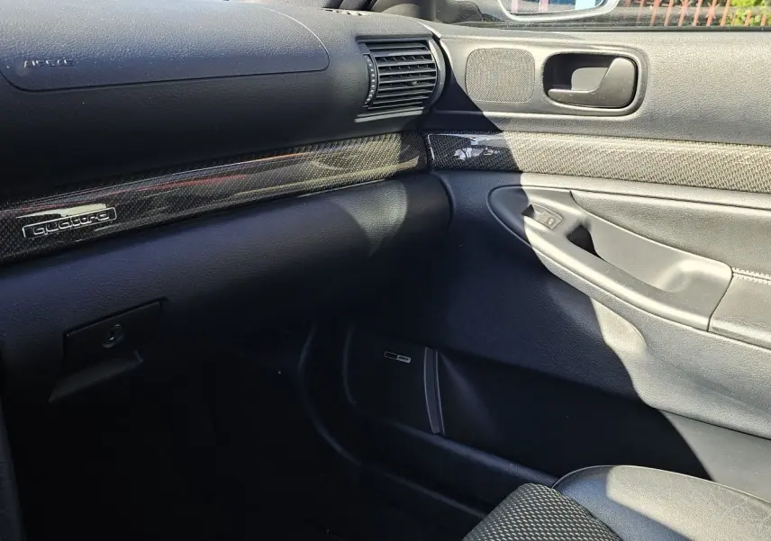 Intérieur côté passager de l'Audi RS4 Avant B5 2001, tableau de bord et porte en cuir noir avec insert carbone Quattro.