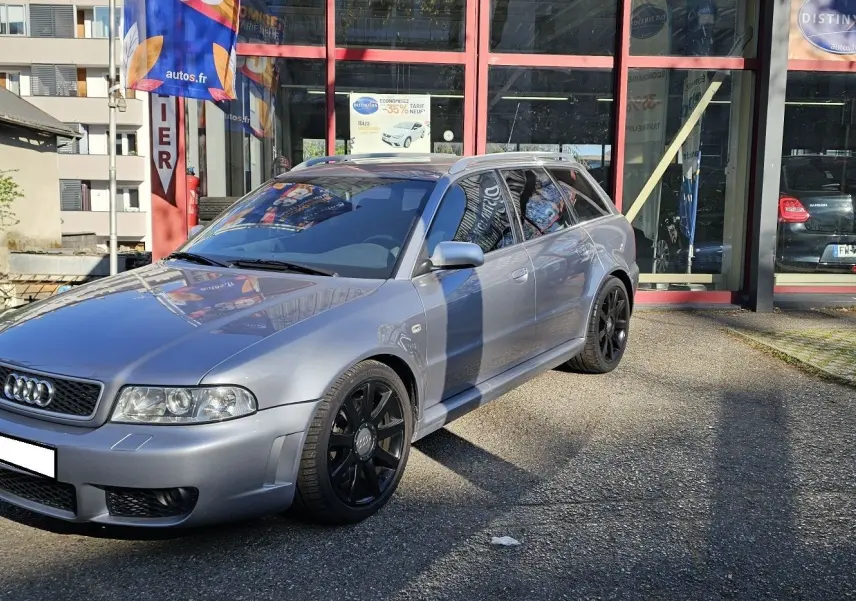 Audi RS4 Avant gris vue 3/4 avant droit, avec jantes noires et carrosserie brillante sous le soleil.