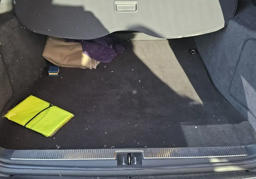 Coffre ouvert d'une Audi RS4 Avant gris 2001, montrant un tapis noir avec un gilet jaune et des vêtements pliés.