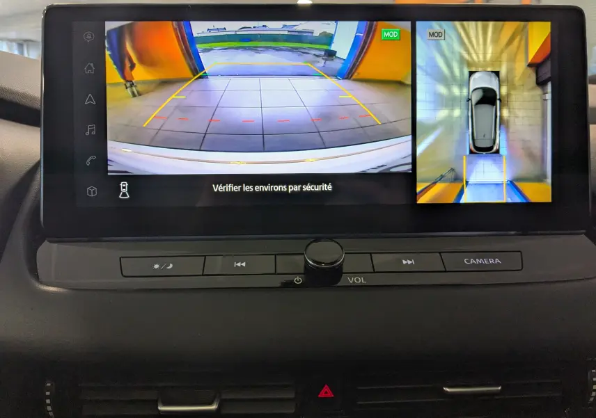 Écran multimédia du Nissan Qashqai blanc 2024 montrant la caméra de recul et la vue 360° en intérieur de garage.