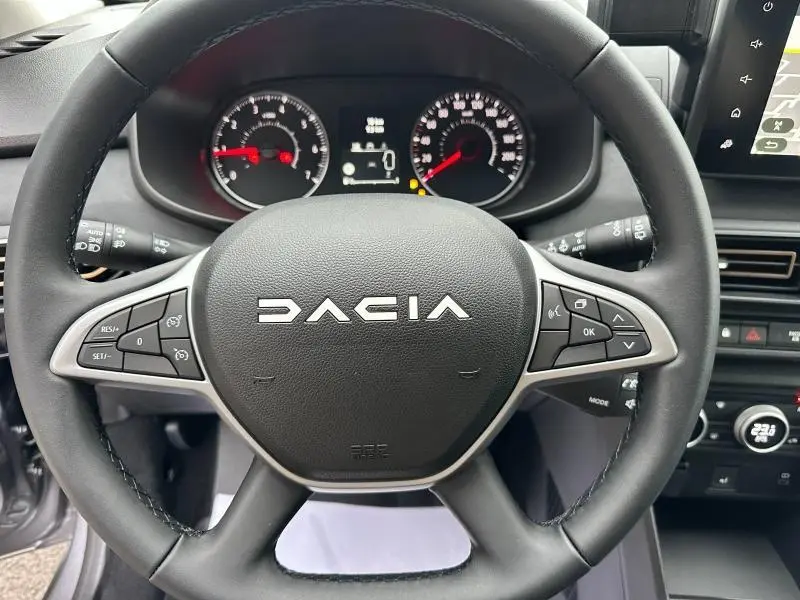 Vue rapprochée du volant noir de la Dacia Jogger 2024 avec commandes intégrées et tableau de bord visible en arrière-plan.