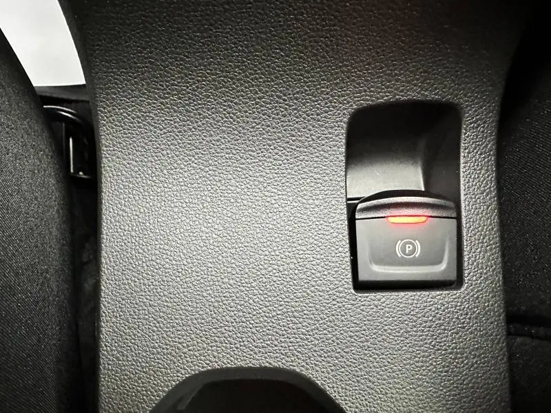 Gros plan sur le bouton de frein de stationnement électrique avec témoin rouge dans l'habitacle gris du Dacia Jogger 2024