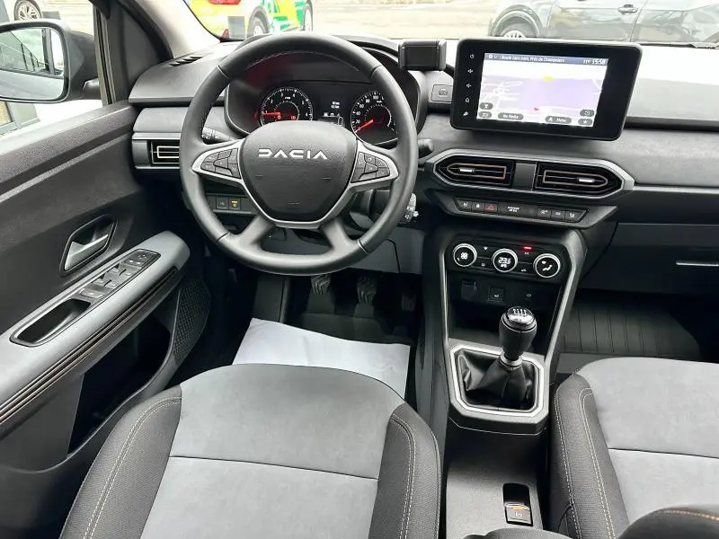 Vue intérieure avant du tableau de bord et volant gris d'une Dacia Jogger 2024 avec écran tactile et boîte manuelle.