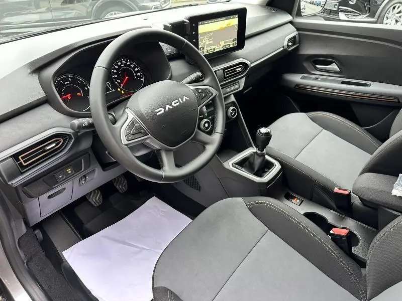 Intérieur avant du Dacia Jogger 2024 avec volant multifonction, écran tactile et sièges gris foncé en tissu.