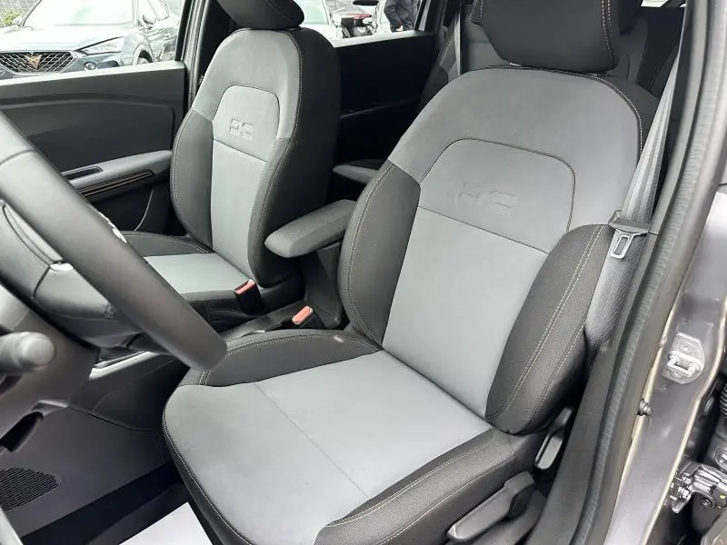 Vue rapprochée des sièges avant gris clair et foncé du Dacia Jogger 2024, avec accoudoir central et logo RC brodé.