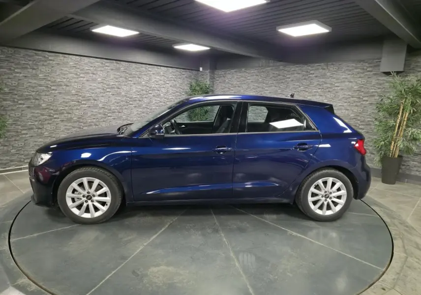 Profil côté gauche d'une Audi A1 Sportback 2024 bleu métallisé avec jantes aluminium 16 pouces dans un showroom.