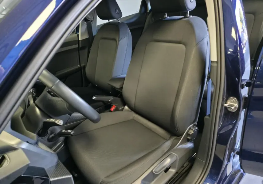 Vue intérieure côté gauche de l'Audi A1 Sportback 2024 bleu, montrant les sièges sport en tissu noir et le volant cuir multifonctions.