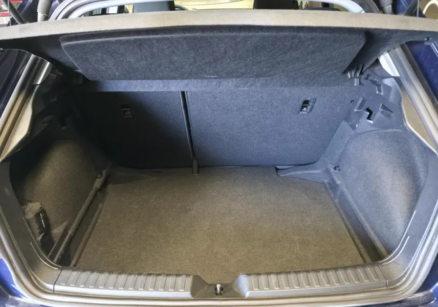 Coffre ouvert d'une Audi A1 Sportback 2024 bleu, montrant l'espace de rangement intérieur et la moquette grise.