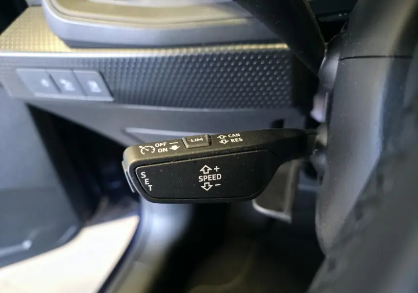 Gros plan sur la commande de régulateur de vitesse à gauche du volant dans l'Audi A1 Sportback bleu 2024.