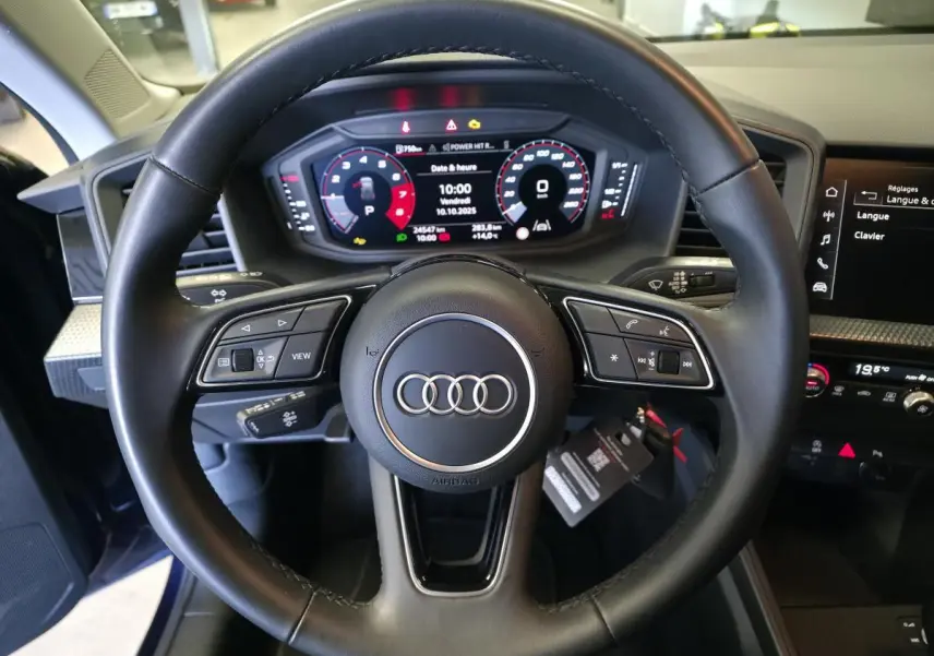 Volant cuir multifonctions Audi A1 Sportback 2024 vu de face avec tableau de bord digital et écran central noir.