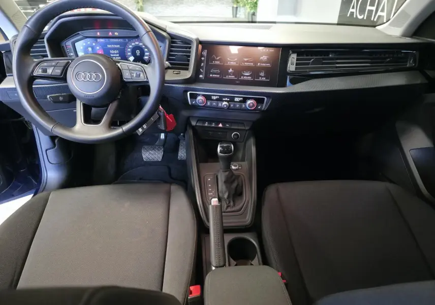 Intérieur de l'Audi A1 Sportback 2024 en vue frontale, tableau de bord noir avec écran digital et volant cuir multifonctions.