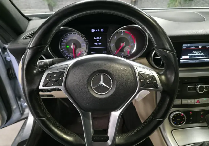 Vue intérieure centrée sur le volant cuir noir de la Mercedes SLK 250 CDI avec tableau de bord et écran multimédia visibles.