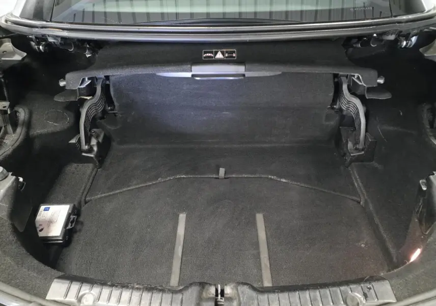Coffre ouvert d'une Mercedes SLK 250 CDI gris, montrant l'espace de rangement avec moquette noire et charnières visibles.