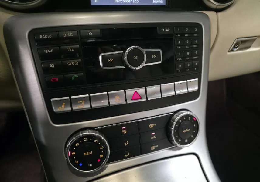 Vue rapprochée de la console centrale argentée avec commandes de climatisation et système audio d'une Mercedes SLK gris intérieur beige.