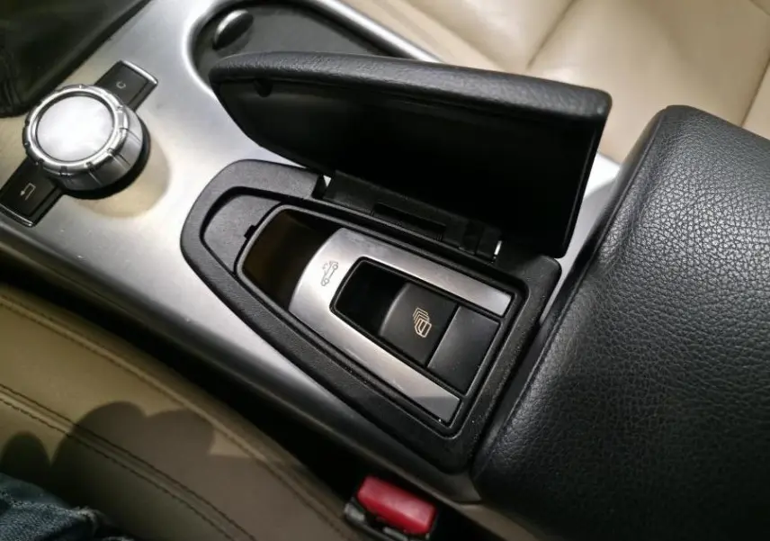 Détail de la console centrale avec accoudoir cuir noir et commandes d'ouverture de coffre et capote sur Mercedes SLK gris.