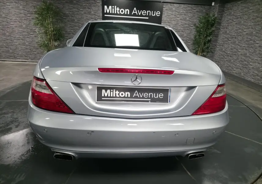 Vue arrière d'une Mercedes SLK gris métallisé avec feux rouges et double sortie d'échappement chromée.
