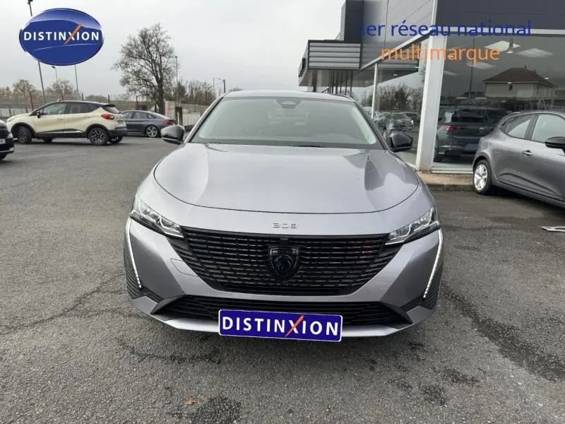 Vue avant d'une Peugeot 308 2024 gris Artense avec calandre noire et logo central distinctif, stationnée devant un showroom.